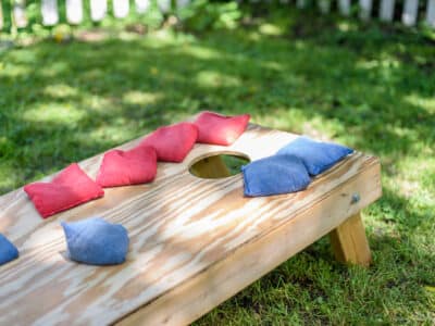 Close-up of a wooden cornhole board with red and blue bean bags on a grassy lawn, ready for a backyard game.