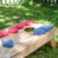 Close-up of a wooden cornhole board with red and blue bean bags on a grassy lawn, ready for a backyard game.