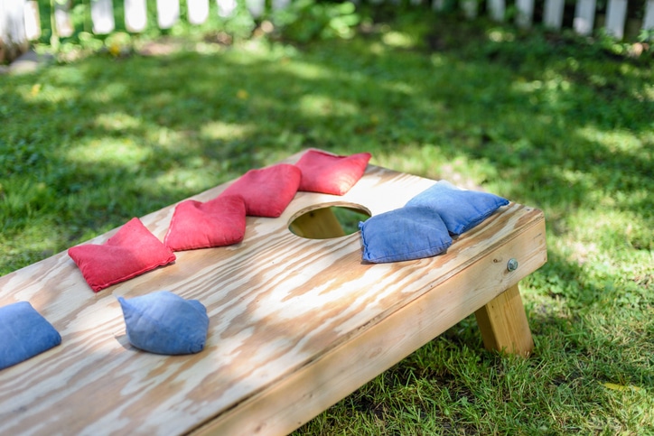 Close-up of a wooden cornhole board with red and blue bean bags on a grassy lawn, ready for a backyard game.